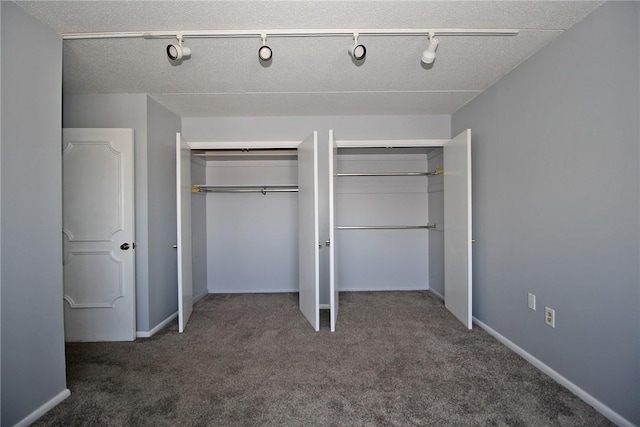 unfurnished bedroom featuring a closet, dark carpet, and rail lighting