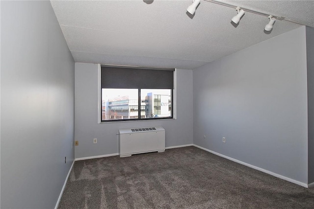 unfurnished room with rail lighting, radiator, and dark colored carpet