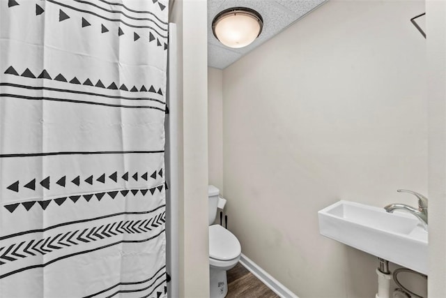 bathroom with toilet, a drop ceiling, hardwood / wood-style flooring, and sink