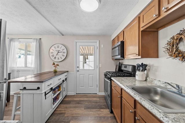 kitchen with a textured ceiling, dark wood-type flooring, stainless steel appliances, sink, and a kitchen breakfast bar