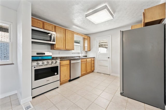 kitchen featuring a textured ceiling, light tile patterned floors, appliances with stainless steel finishes, and sink