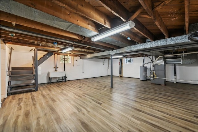 basement featuring heating unit, water heater, sink, and hardwood / wood-style flooring