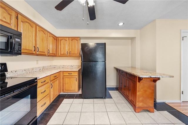 kitchen featuring light stone countertops, black appliances, kitchen peninsula, a breakfast bar, and light tile patterned floors