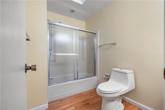 bathroom featuring toilet, bath / shower combo with glass door, and wood-type flooring