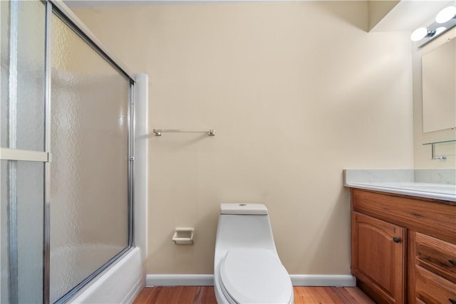 full bathroom featuring wood-type flooring, bath / shower combo with glass door, toilet, and vanity