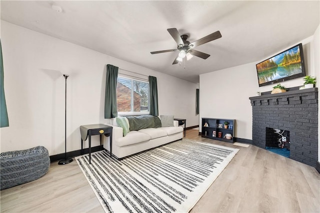 living room with ceiling fan, a brick fireplace, and light hardwood / wood-style flooring