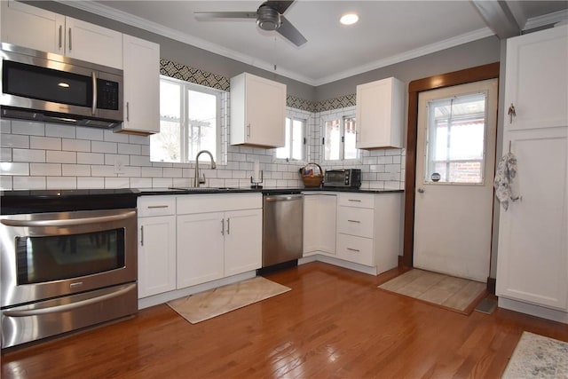 kitchen featuring appliances with stainless steel finishes, dark wood-type flooring, white cabinetry, decorative backsplash, and sink