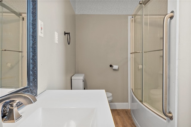 full bathroom with wood-type flooring, combined bath / shower with glass door, toilet, a textured ceiling, and vanity