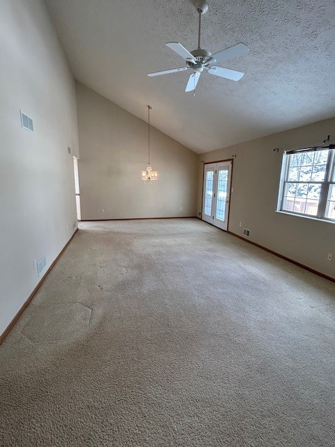 spare room featuring french doors, ceiling fan with notable chandelier, a textured ceiling, and light carpet