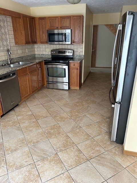 kitchen with a textured ceiling, stainless steel appliances, decorative backsplash, sink, and light tile patterned floors