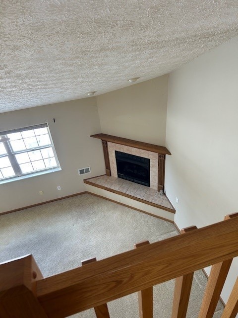 unfurnished living room with carpet, a textured ceiling, and a tiled fireplace