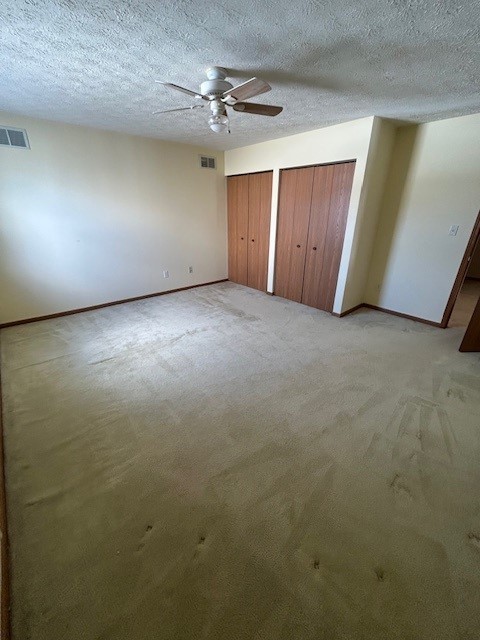 unfurnished bedroom featuring light carpet, multiple closets, a textured ceiling, and ceiling fan