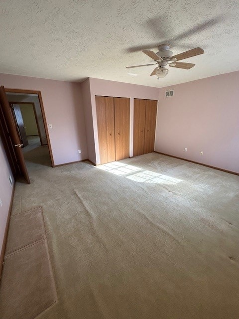 unfurnished bedroom with ceiling fan, two closets, a textured ceiling, and light carpet