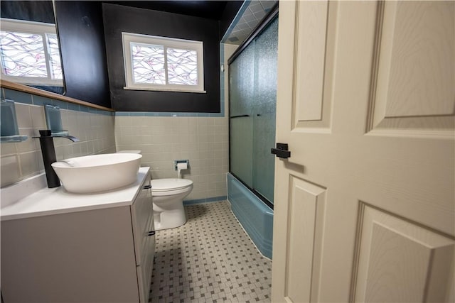 full bathroom with a wealth of natural light, enclosed tub / shower combo, vanity, tile walls, and toilet