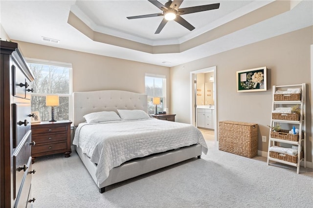 bedroom featuring ceiling fan, multiple windows, connected bathroom, and a tray ceiling