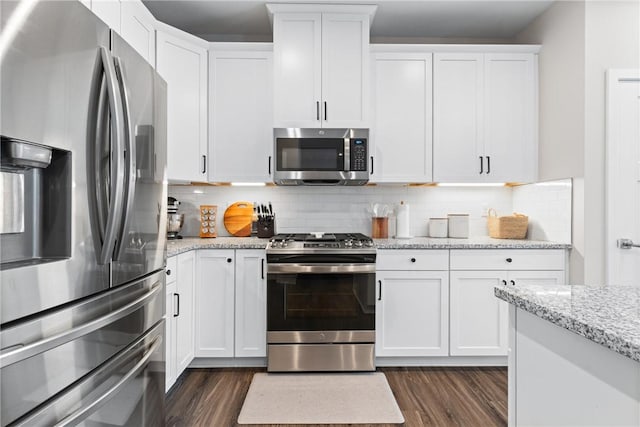 kitchen featuring light stone countertops, white cabinetry, dark wood-type flooring, backsplash, and stainless steel appliances