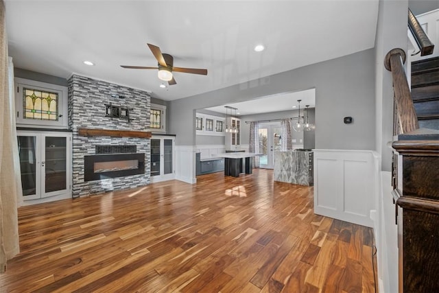 unfurnished living room featuring hardwood / wood-style flooring, ceiling fan with notable chandelier, french doors, and a fireplace