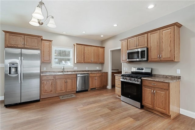 kitchen featuring decorative light fixtures, sink, light wood-type flooring, and stainless steel appliances