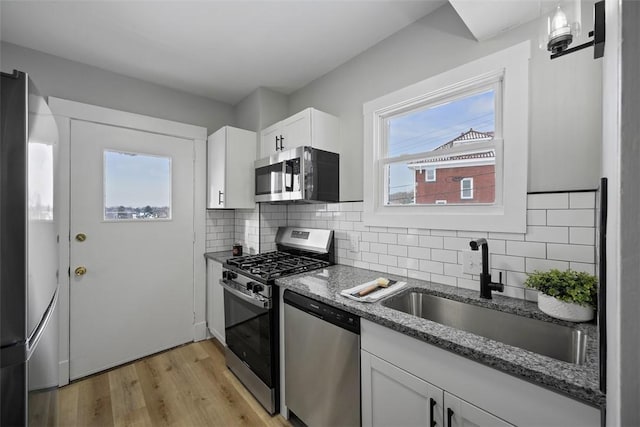 kitchen with appliances with stainless steel finishes, tasteful backsplash, white cabinetry, sink, and dark stone counters