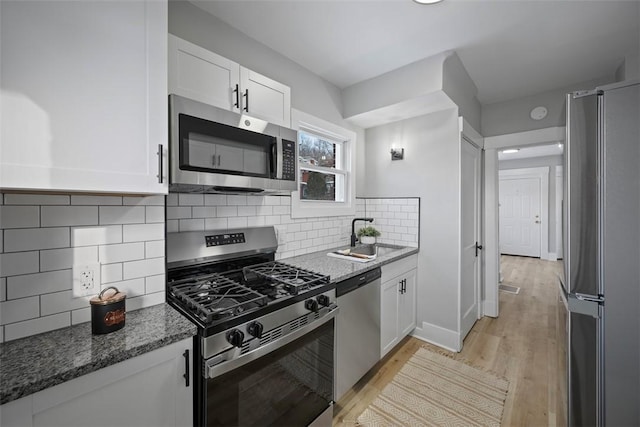 kitchen featuring dark stone counters, white cabinets, light wood-type flooring, sink, and stainless steel appliances