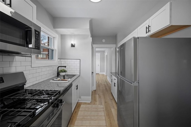 kitchen featuring light stone countertops, white cabinetry, stainless steel appliances, sink, and light hardwood / wood-style flooring