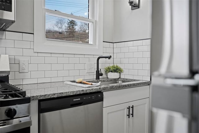 kitchen with appliances with stainless steel finishes, white cabinetry, decorative backsplash, sink, and light stone counters