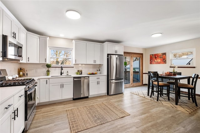 kitchen with sink, stainless steel appliances, white cabinetry, and light wood-type flooring