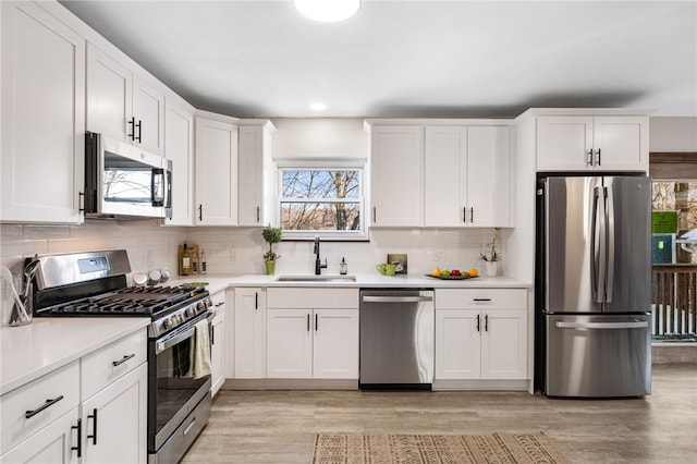 kitchen featuring appliances with stainless steel finishes, white cabinetry, decorative backsplash, sink, and light hardwood / wood-style flooring