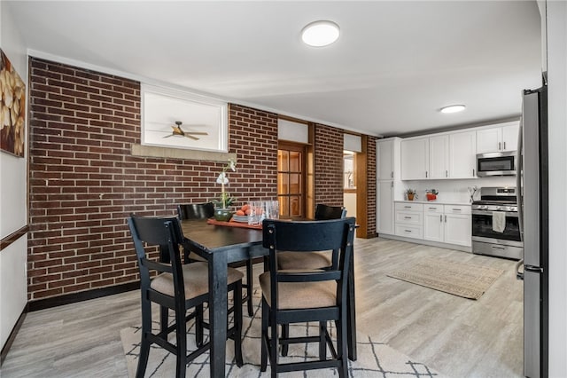 dining area featuring light wood-type flooring, brick wall, and ceiling fan