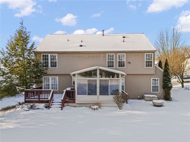 snow covered house featuring a wooden deck and a sunroom