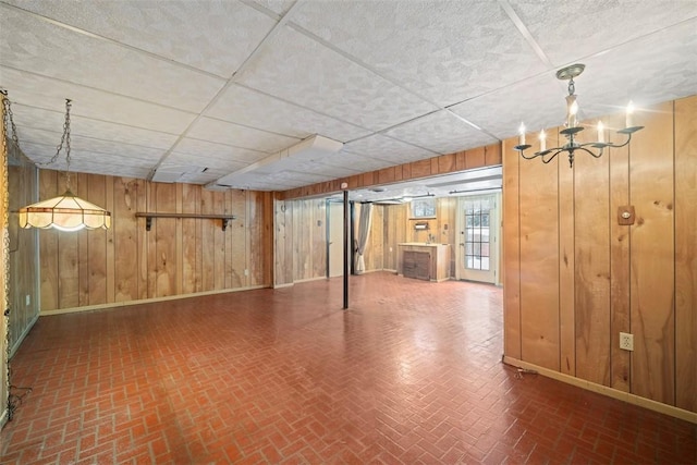 basement featuring a drop ceiling, a chandelier, and wooden walls