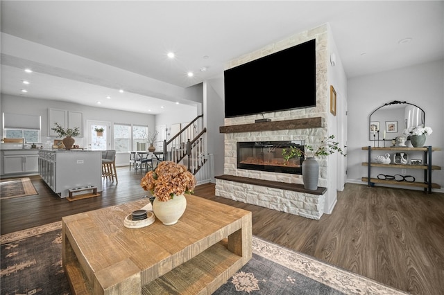 living room featuring a stone fireplace and dark wood-type flooring