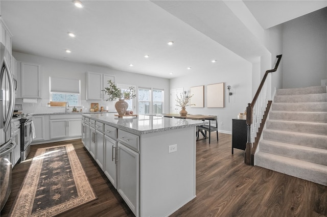 kitchen with stainless steel range oven, a kitchen island, backsplash, dark hardwood / wood-style floors, and light stone counters