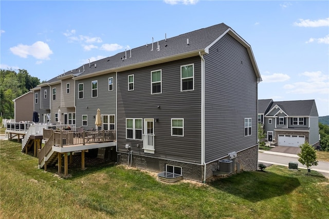 back of property featuring central AC unit, a lawn, a wooden deck, and a garage