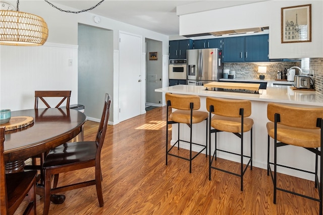 kitchen featuring a kitchen bar, blue cabinetry, wood-type flooring, stainless steel refrigerator with ice dispenser, and kitchen peninsula