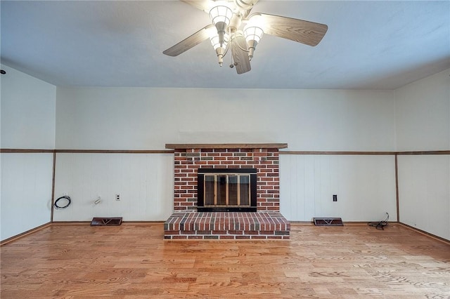 unfurnished living room featuring a brick fireplace, ceiling fan, and light wood-type flooring