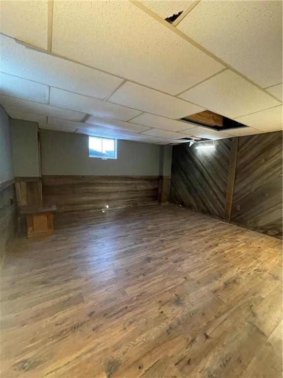 basement featuring a paneled ceiling, wood walls, and hardwood / wood-style floors