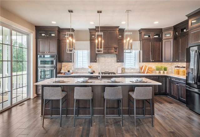 kitchen featuring pendant lighting, appliances with stainless steel finishes, dark hardwood / wood-style flooring, a kitchen island with sink, and dark brown cabinets