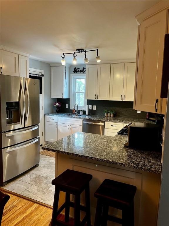 kitchen featuring white cabinets, stainless steel appliances, dark stone counters, kitchen peninsula, and a breakfast bar area