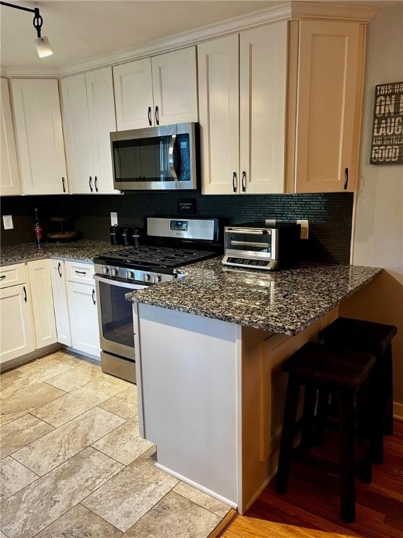 kitchen with appliances with stainless steel finishes, white cabinetry, dark stone countertops, rail lighting, and kitchen peninsula