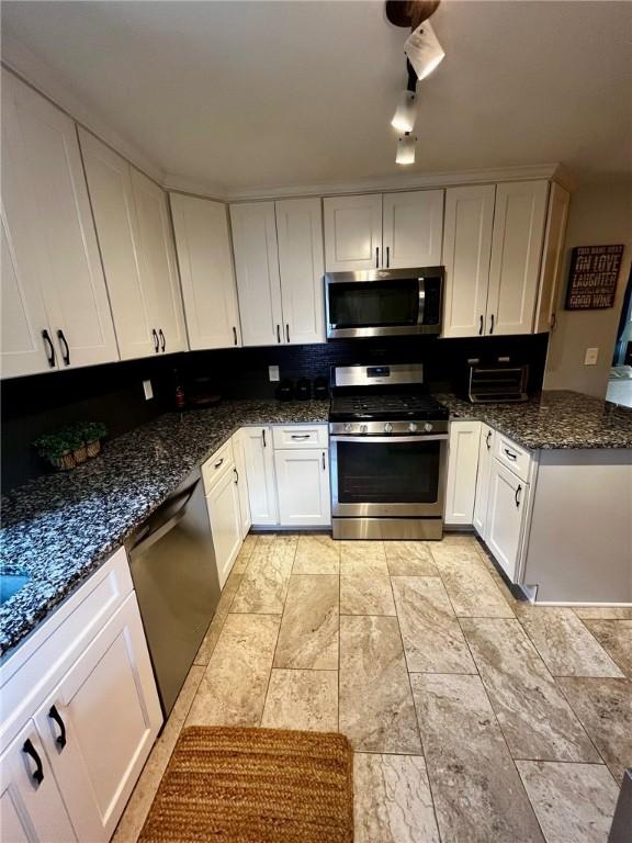 kitchen with appliances with stainless steel finishes, track lighting, white cabinetry, dark stone countertops, and backsplash