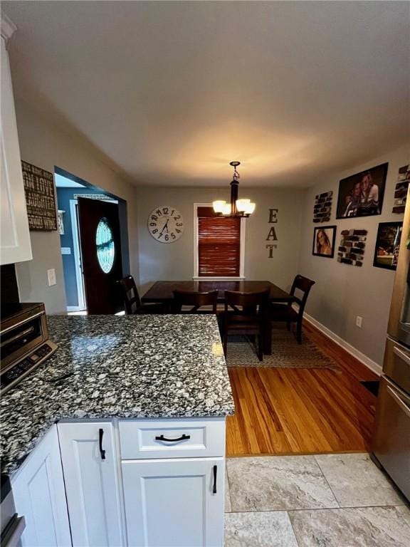 kitchen with a chandelier, dark stone countertops, white cabinetry, and pendant lighting