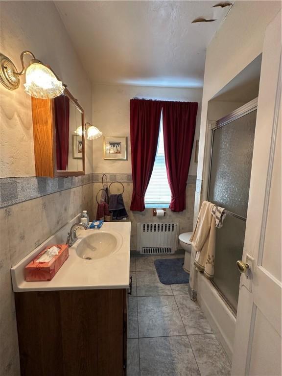 full bathroom featuring toilet, tile walls, radiator heating unit, vanity, and enclosed tub / shower combo