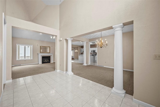 unfurnished living room with a notable chandelier, a high ceiling, ornate columns, and light carpet