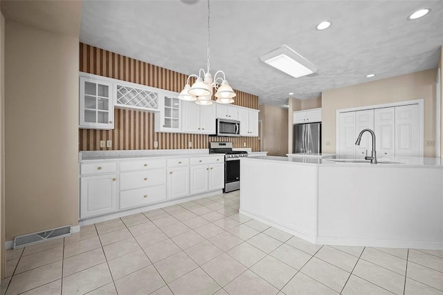 kitchen with pendant lighting, appliances with stainless steel finishes, sink, white cabinets, and a notable chandelier