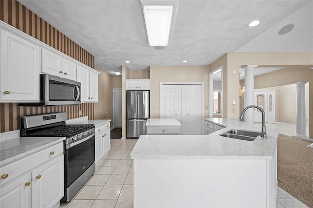 kitchen with appliances with stainless steel finishes, decorative columns, sink, white cabinets, and a center island with sink