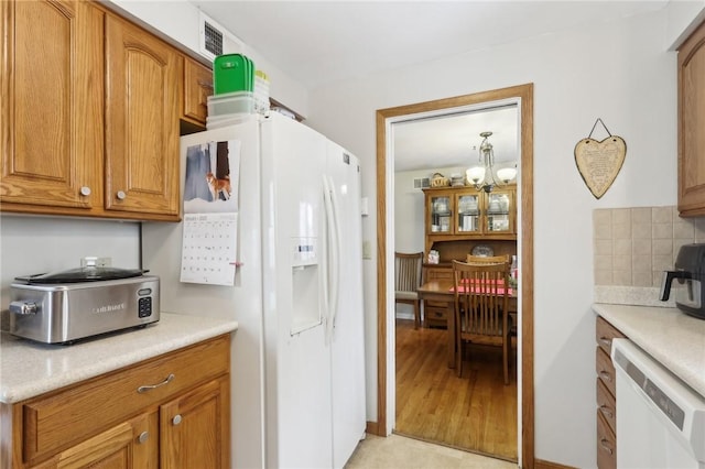 kitchen featuring white appliances, decorative backsplash, and an inviting chandelier