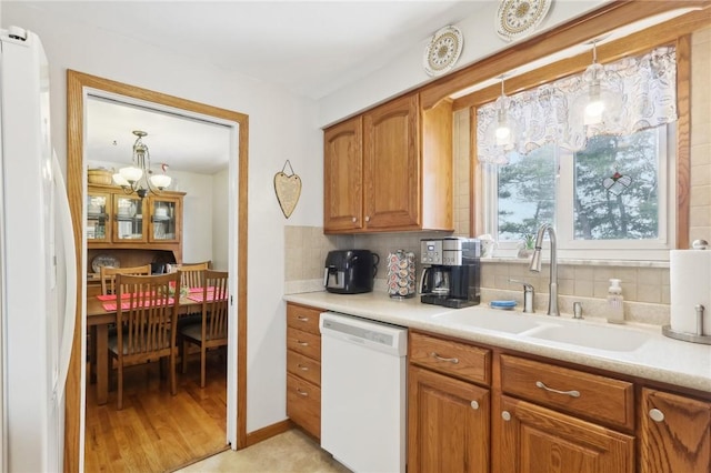 kitchen with white appliances, decorative backsplash, sink, light wood-type flooring, and pendant lighting