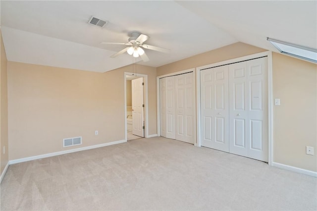 unfurnished bedroom with vaulted ceiling with skylight, light carpet, ceiling fan, ensuite bathroom, and multiple closets