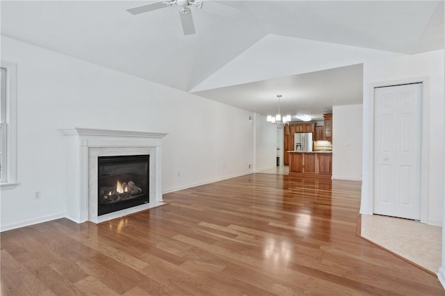 unfurnished living room with ceiling fan with notable chandelier, lofted ceiling, a premium fireplace, and light wood-type flooring